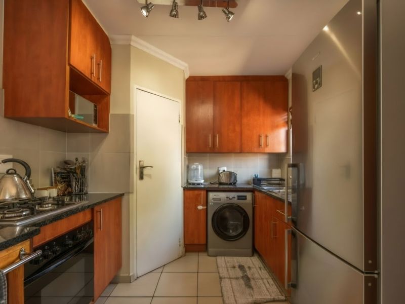 A functional kitchen featuring warm-toned wooden cabinetry, granite countertops, a gas hob, and integrated space for laundry appliances.