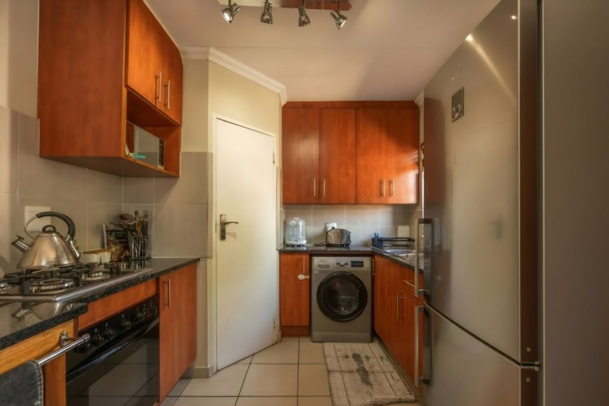 A functional kitchen featuring warm-toned wooden cabinetry, granite countertops, a gas hob, and integrated space for laundry appliances.