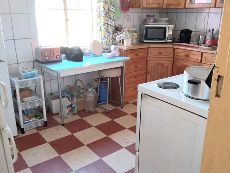 A functional kitchen featuring traditional wooden cabinetry, tiled splashbacks, and a classic checkerboard floor, offering potential for a modern renovation.