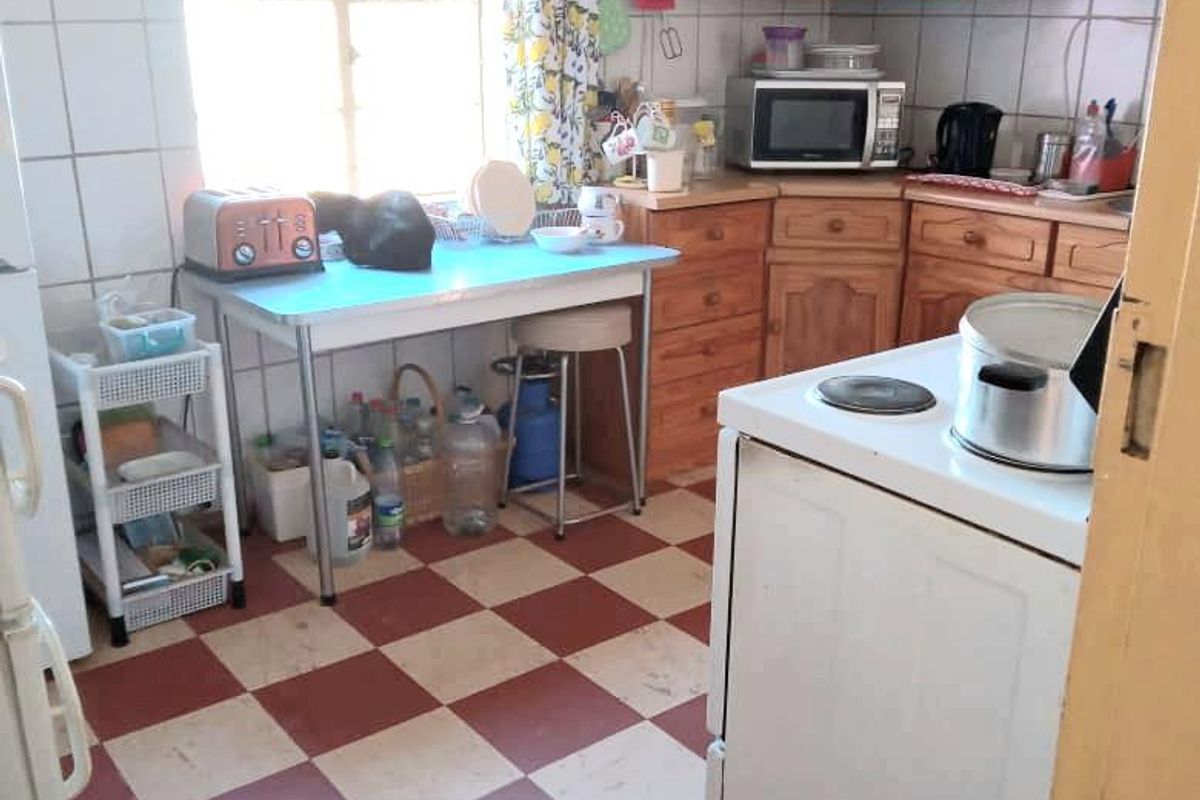 A functional kitchen featuring traditional wooden cabinetry, tiled splashbacks, and a classic checkerboard floor, offering potential for a modern renovation.