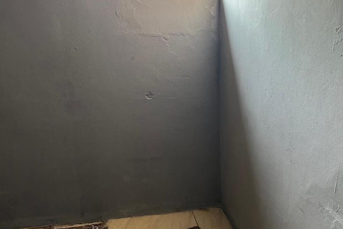 An unfinished interior space featuring exposed plaster walls, a small window, and damaged floor tiling in need of renovation.