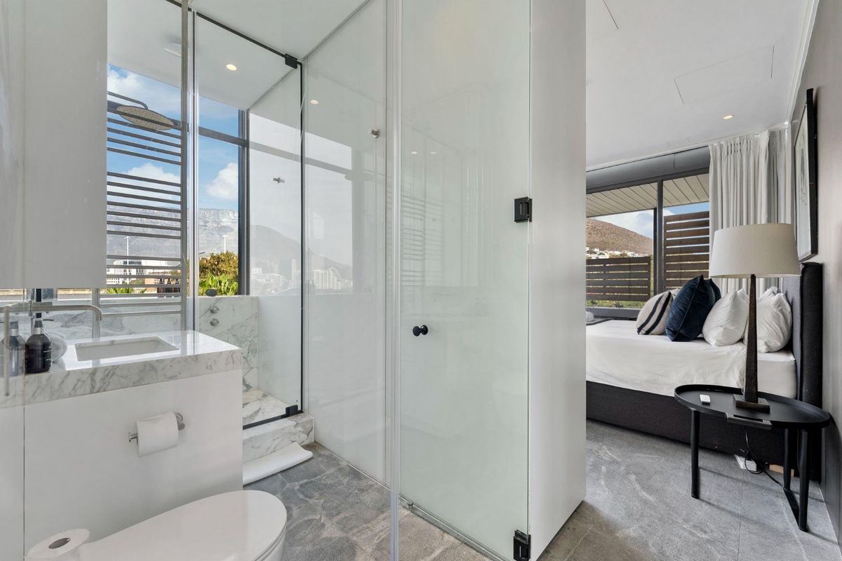 Modern open-plan bedroom featuring an integrated en-suite bathroom with a glass shower enclosure, marble vanity, and high-quality stone flooring with mountain views.