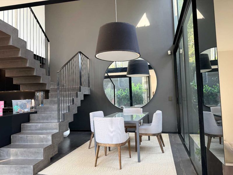 Modern dining area featuring a striking concrete staircase, floor-to-ceiling glass walls, and high ceilings, creating a sophisticated and open architectural space.