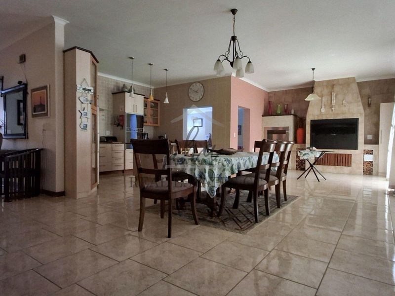 Spacious open-plan living and dining area featuring tiled flooring, a prominent built-in fireplace, and an integrated kitchen with cabinetry.