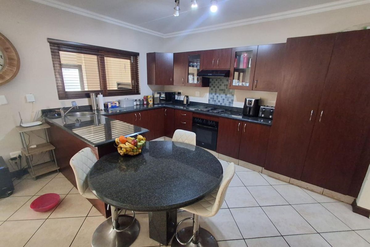 A functional kitchen featuring dark wood cabinetry, granite countertops, a built-in oven with extractor fan, and a breakfast nook area with tiled flooring.