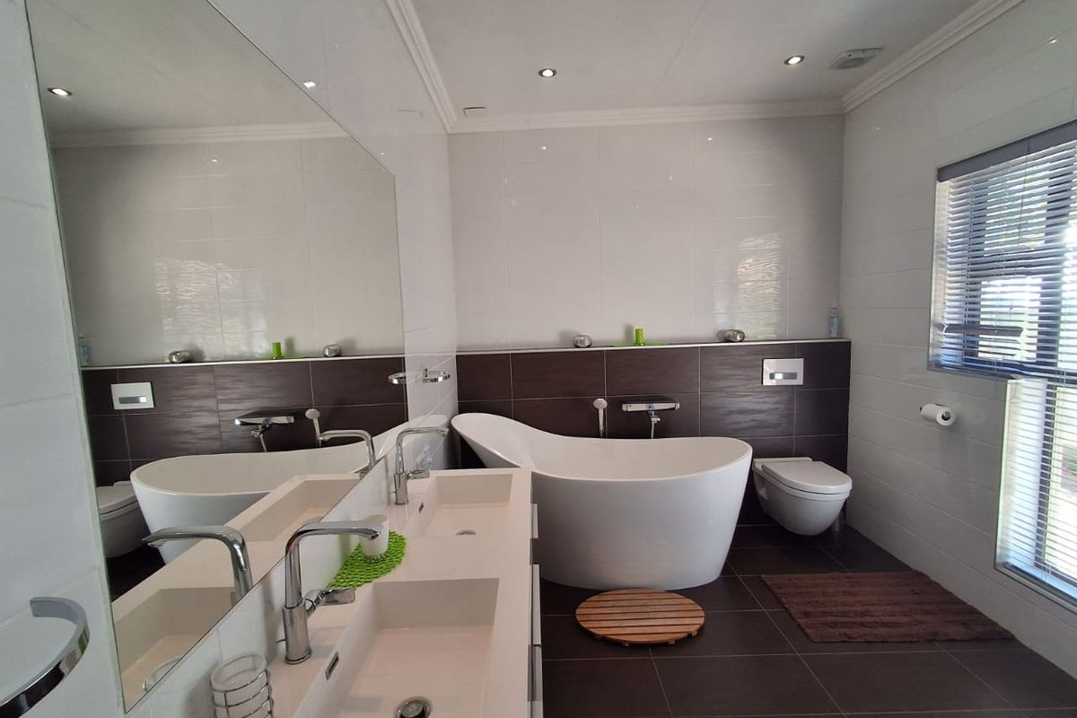Modern bathroom featuring a freestanding bathtub, wall-mounted toilet, and a double vanity with integrated sinks and a large wall-to-wall mirror.