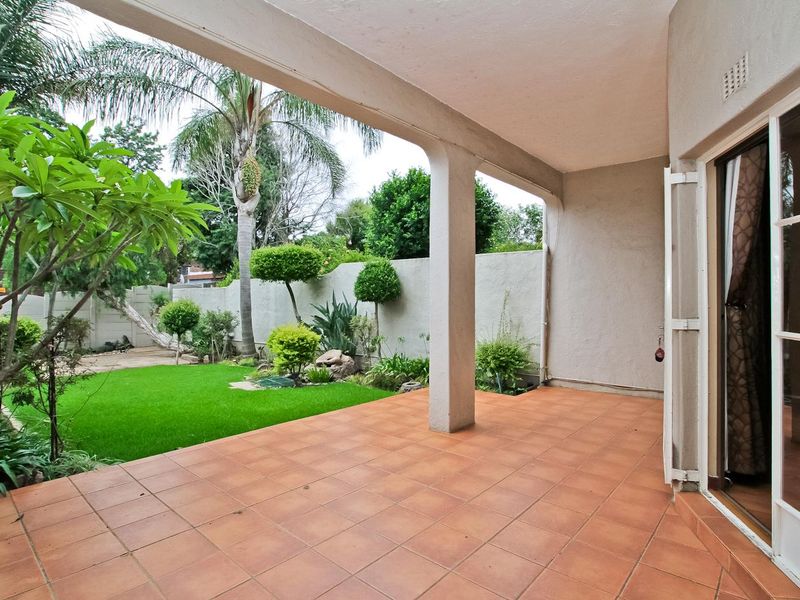 A covered patio featuring tiled flooring and a concrete support pillar, overlooking a private garden with a boundary wall.