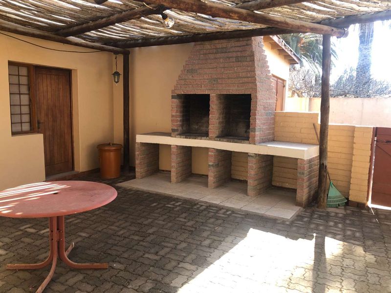 Covered outdoor patio area featuring a built-in brick braai, paved flooring, and a rustic timber pergola structure.
