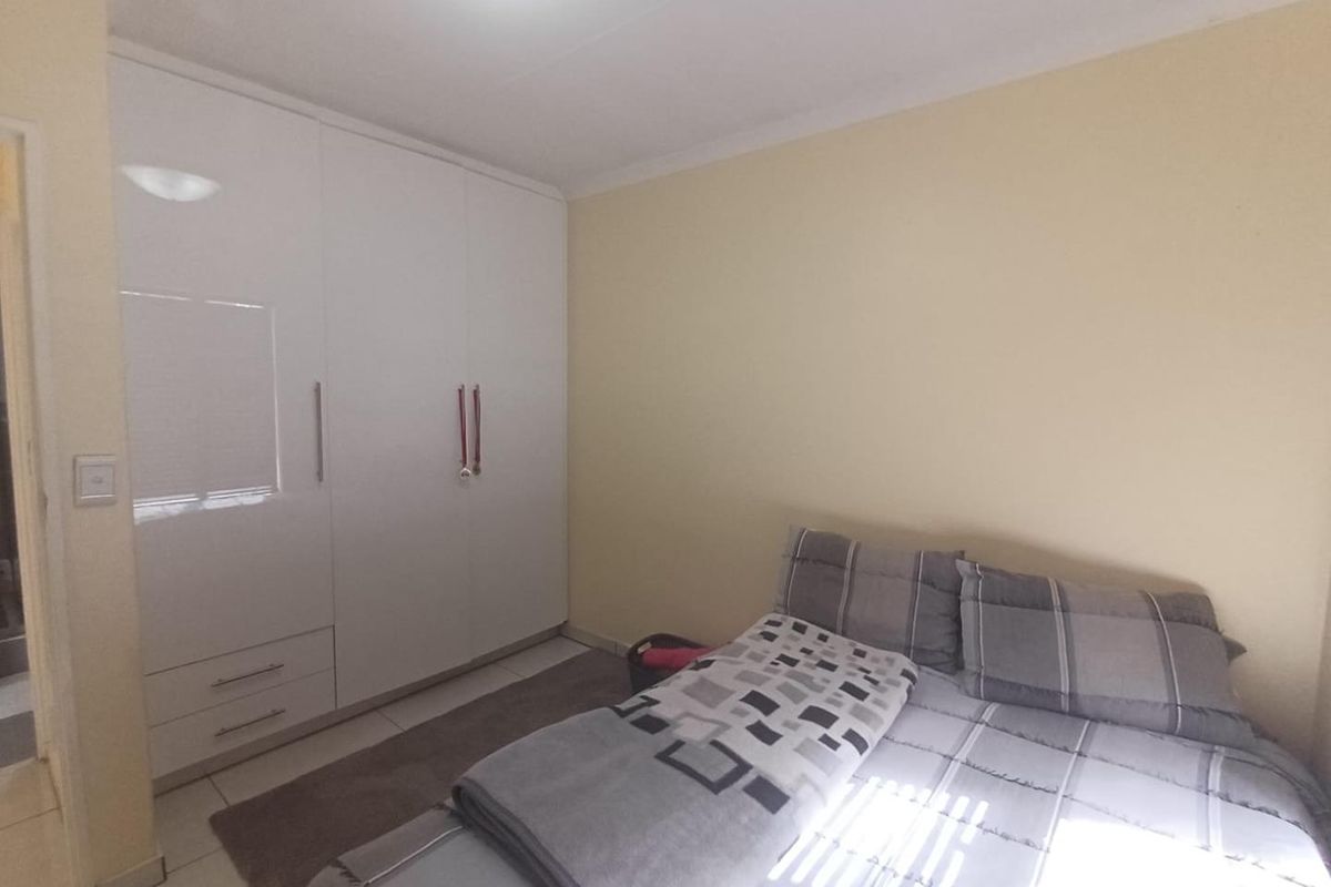 A functional bedroom featuring built-in white cupboards, tiled flooring, and neutral wall finishes, providing a clean and practical living space.
