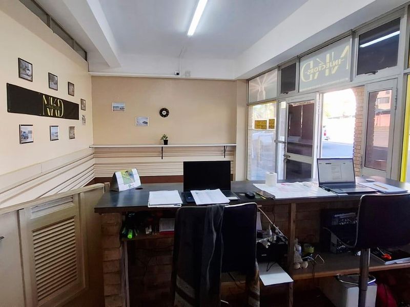 Functional office space featuring a built-in reception desk, large glass storefront windows, and fluorescent lighting, suitable for a professional business environment.