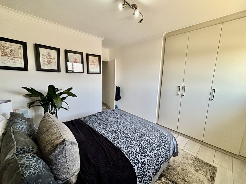 A well-maintained bedroom featuring neutral walls, tiled flooring, and ample storage with a large built-in wardrobe.