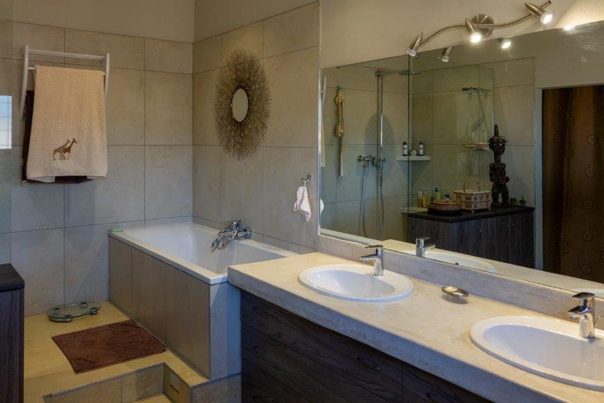 A well-maintained bathroom featuring a double vanity with stone countertop, a built-in bathtub, and a large wall-to-wall mirror with integrated lighting.