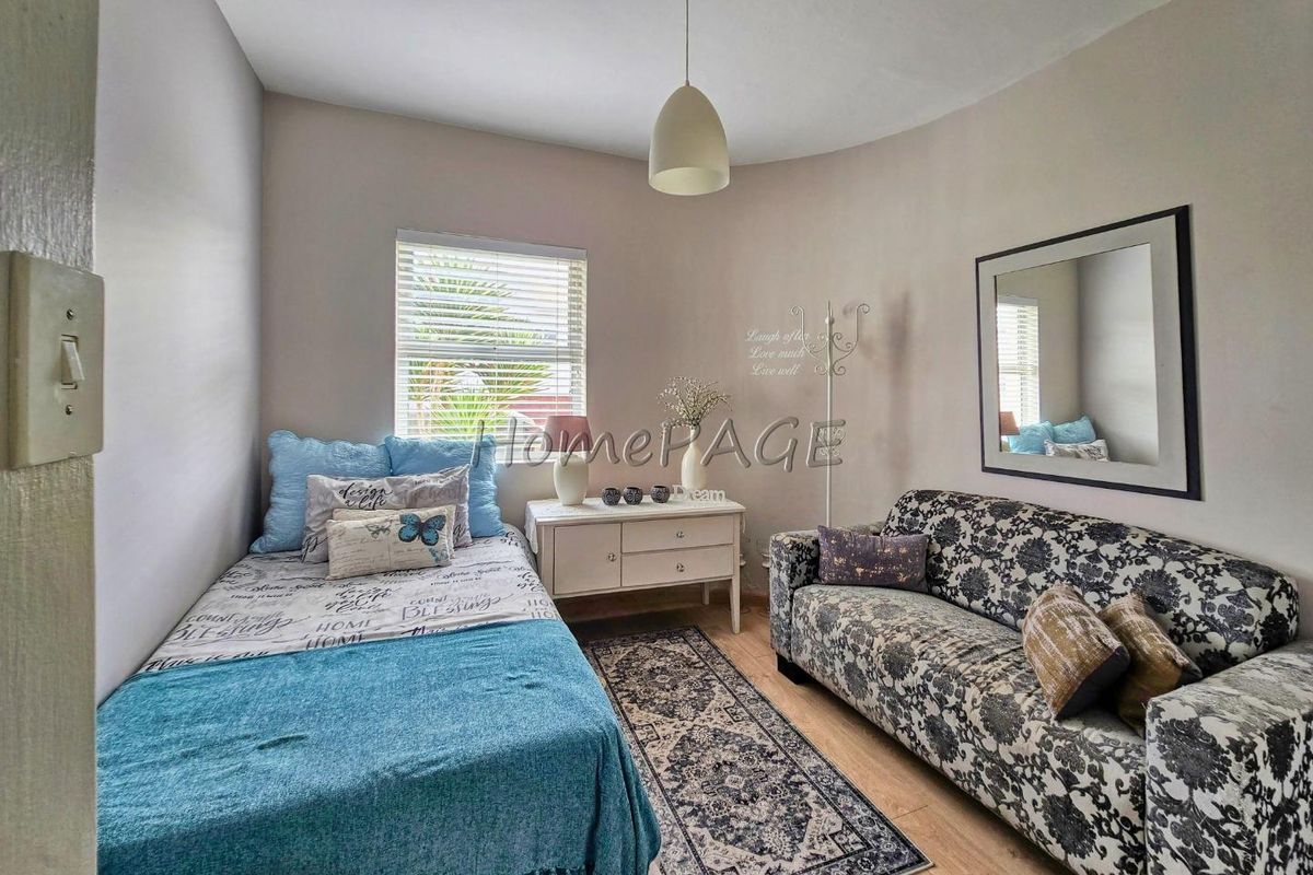 A compact bedroom featuring laminate flooring, a pendant light fixture, and venetian blinds, offering a functional space with neutral wall tones.