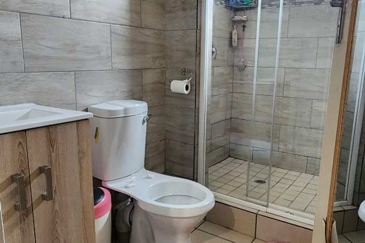 A functional bathroom featuring a glass-enclosed shower, a modern vanity cabinet, and neutral wall tiling.
