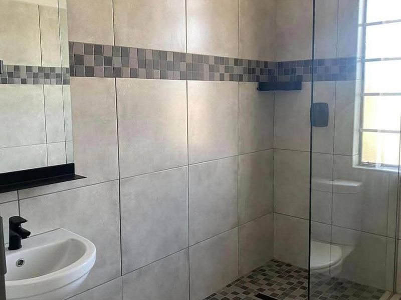 Modern bathroom featuring a walk-in shower with glass screen, rain shower head, wall-mounted basin, and contemporary mosaic tile accents.