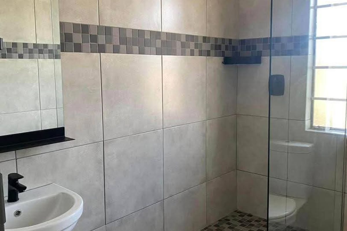 Modern bathroom featuring a walk-in shower with glass screen, rain shower head, wall-mounted basin, and contemporary mosaic tile accents.