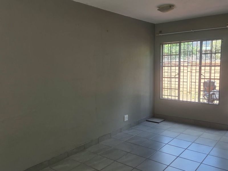 A vacant bedroom featuring neutral tiled flooring, a large window with security bars, and a simple flush mount ceiling light.