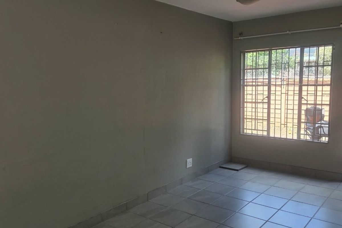 A vacant bedroom featuring neutral tiled flooring, a large window with security bars, and a simple flush mount ceiling light.