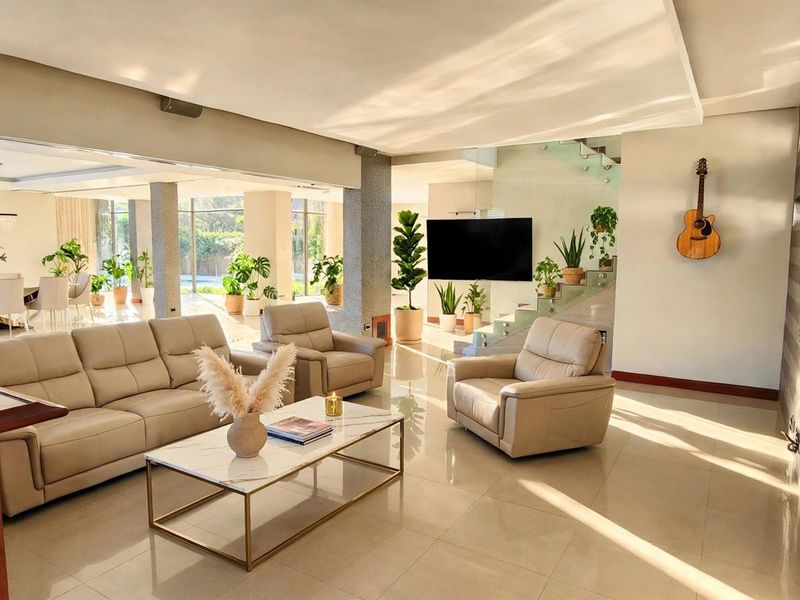 Spacious open-plan living area featuring polished tile floors, modern recessed lighting, a glass staircase, and seamless flow to the outdoor patio area.