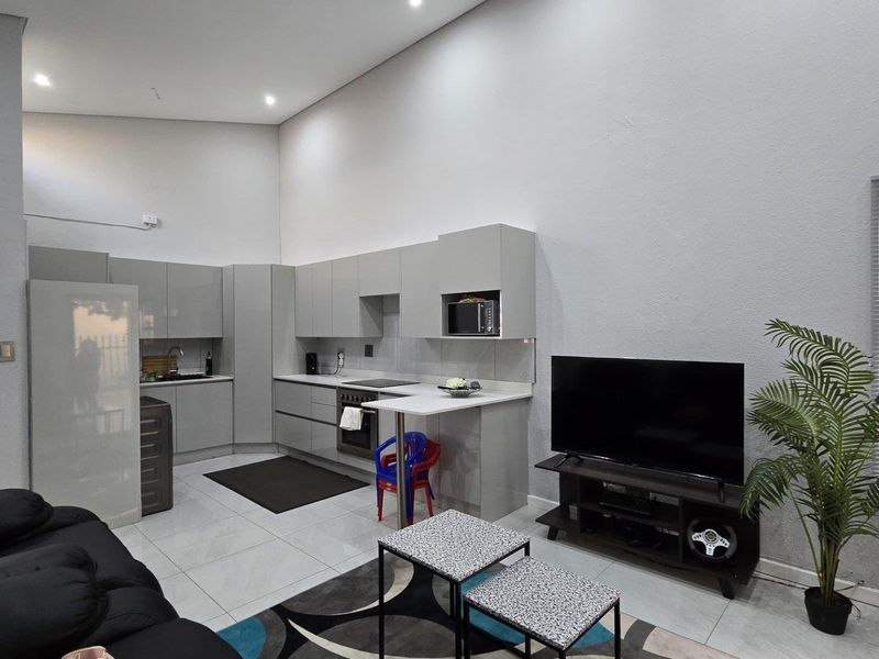Modern open-plan living area featuring a sleek kitchen with built-in cabinetry, integrated appliances, high ceilings, and tiled flooring throughout.