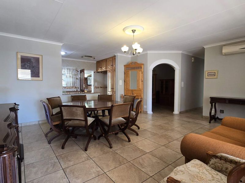 Spacious open-plan living and dining area featuring tiled floors, a decorative archway, and a wall-mounted air conditioning unit.