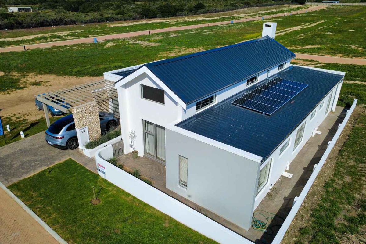 Aerial view of a modern house featuring a dark metal roof, integrated solar panels, a stone-clad entrance pillar, and a covered carport.