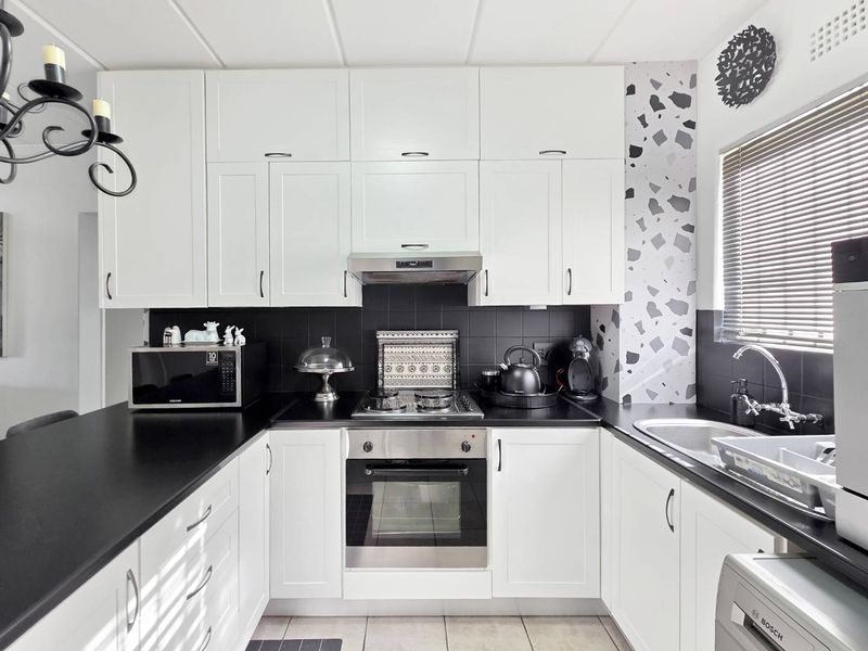 A modern, well-maintained kitchen featuring white cabinetry, black countertops, a stainless steel oven, gas hob, and a stylish terrazzo-patterned accent wall.
