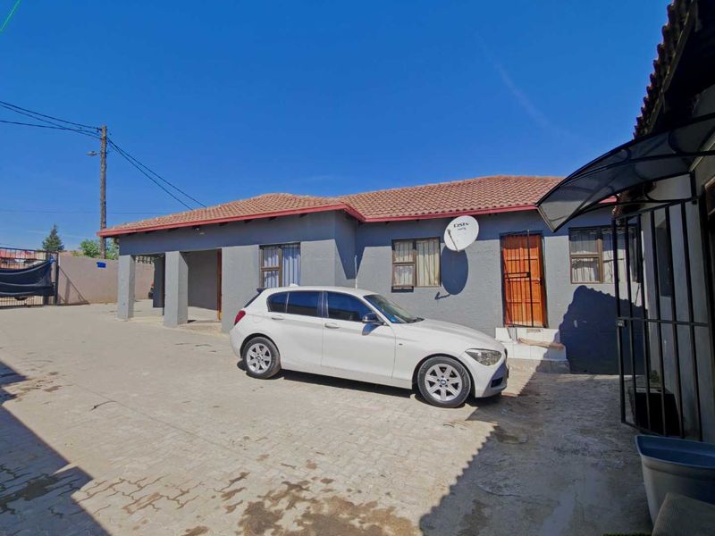 Front exterior view of a single-story house featuring a paved driveway, tiled roof, and security features including burglar bars and a security gate.