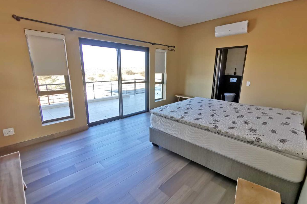 Spacious bedroom featuring wood-look flooring, sliding glass doors leading to a balcony, and an en-suite bathroom with air conditioning unit.