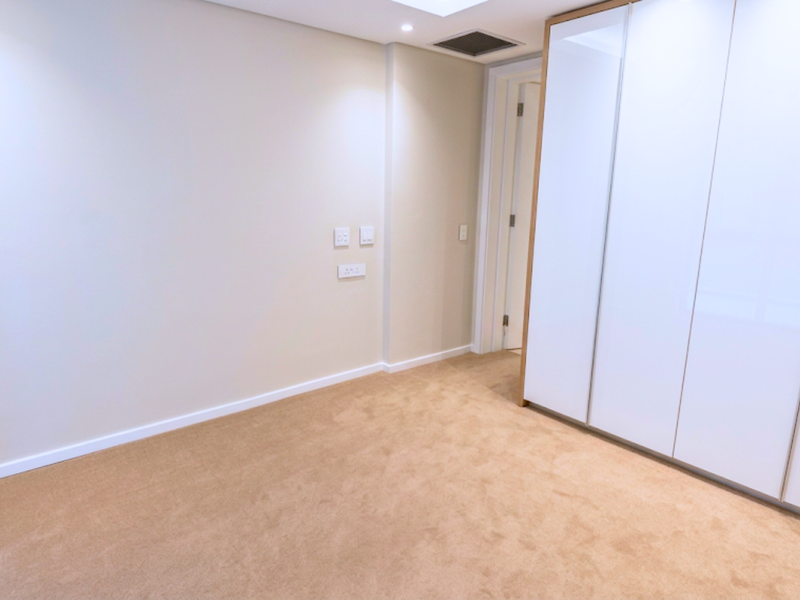 A bright, empty bedroom featuring neutral carpeting, recessed ceiling lighting, and modern floor-to-ceiling built-in cupboards with a clean, minimalist finish.