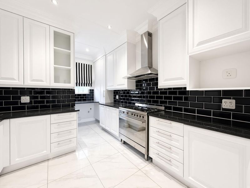 Modern kitchen featuring white shaker cabinetry, contrasting black subway tile backsplash, black granite countertops, and high-quality stainless steel gas range and extractor fan.