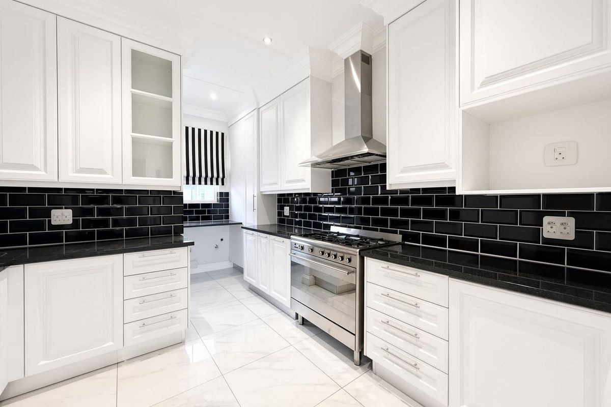 Modern kitchen featuring white shaker cabinetry, contrasting black subway tile backsplash, black granite countertops, and high-quality stainless steel gas range and extractor fan.