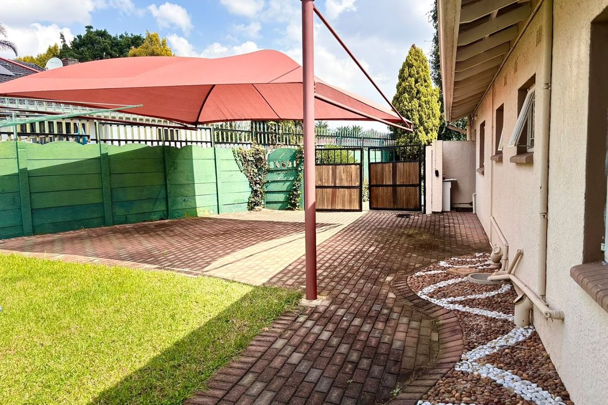 Rear exterior area featuring a paved driveway, shade sail structure, and perimeter walling with gated access.
