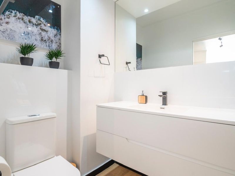 Modern bathroom featuring a sleek wall-mounted vanity with integrated basin, black fixtures, large mirror, and a dual-flush toilet in a clean, contemporary finish.