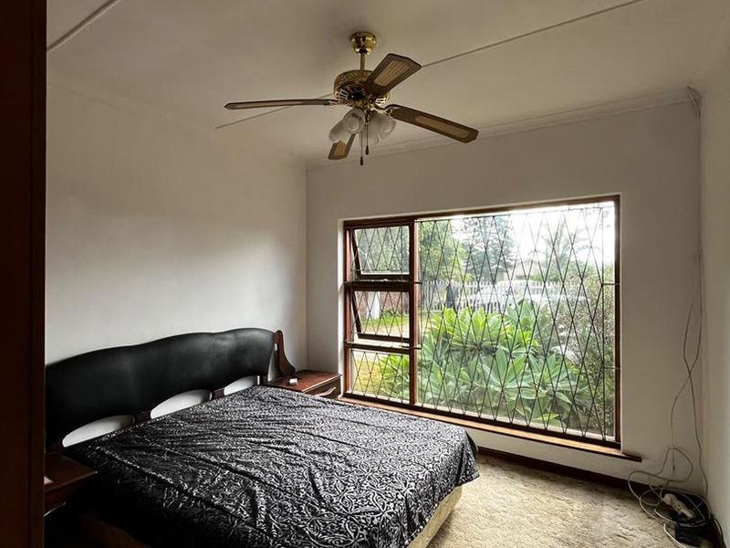 A bedroom featuring a ceiling fan, large window with security bars, and carpet flooring.