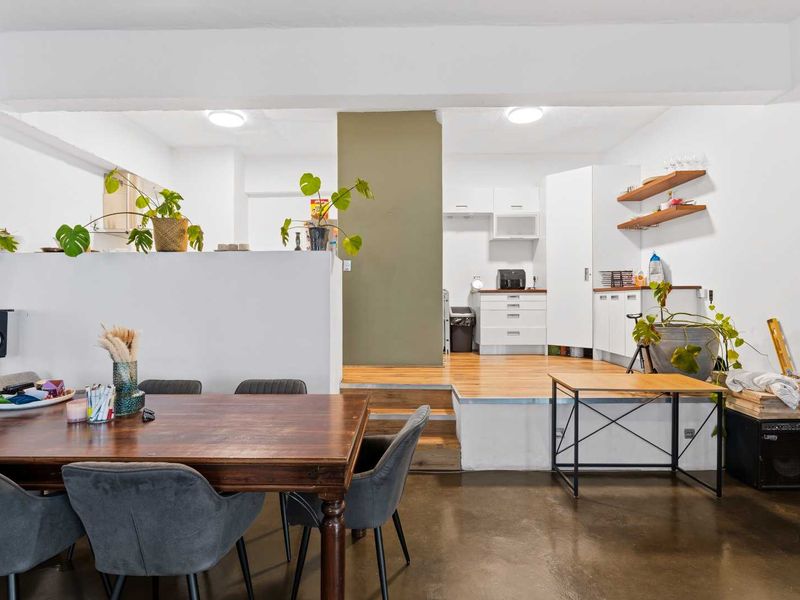 Open plan office space featuring a raised timber platform, polished concrete floors, and built-in kitchen cabinetry with floating shelving.
