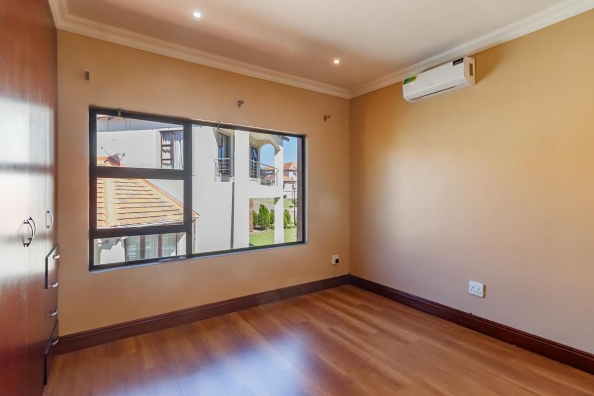 A bright, empty bedroom featuring warm-toned laminate flooring, built-in wooden cupboards, and a wall-mounted air conditioning unit.