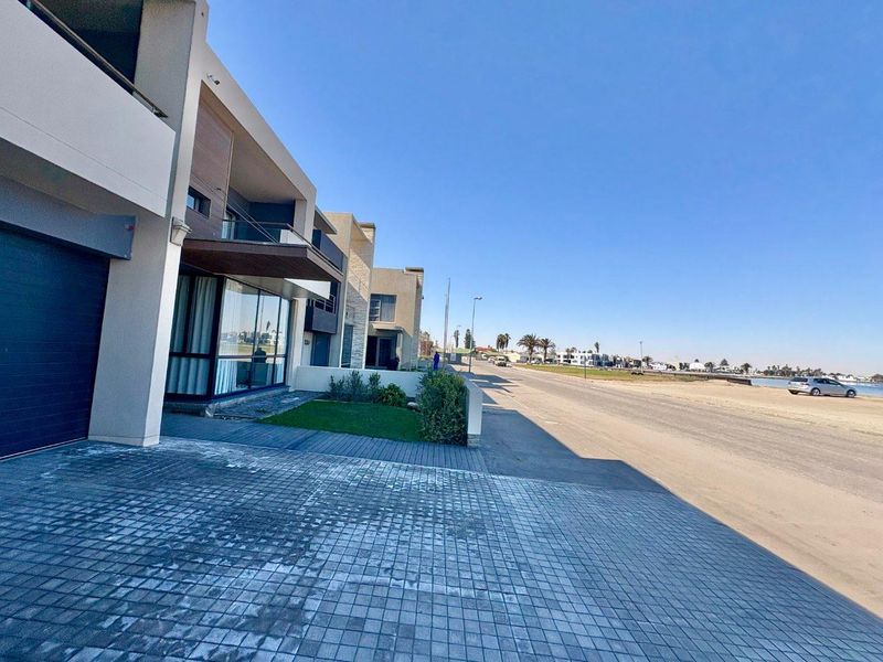 Modern multi-story residential property featuring a paved driveway, integrated garage, and balcony, situated in a prime coastal location.
