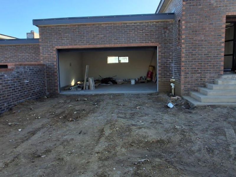 Front exterior view of a brick house under construction, featuring a garage, concrete entrance steps, and an unfinished yard area.