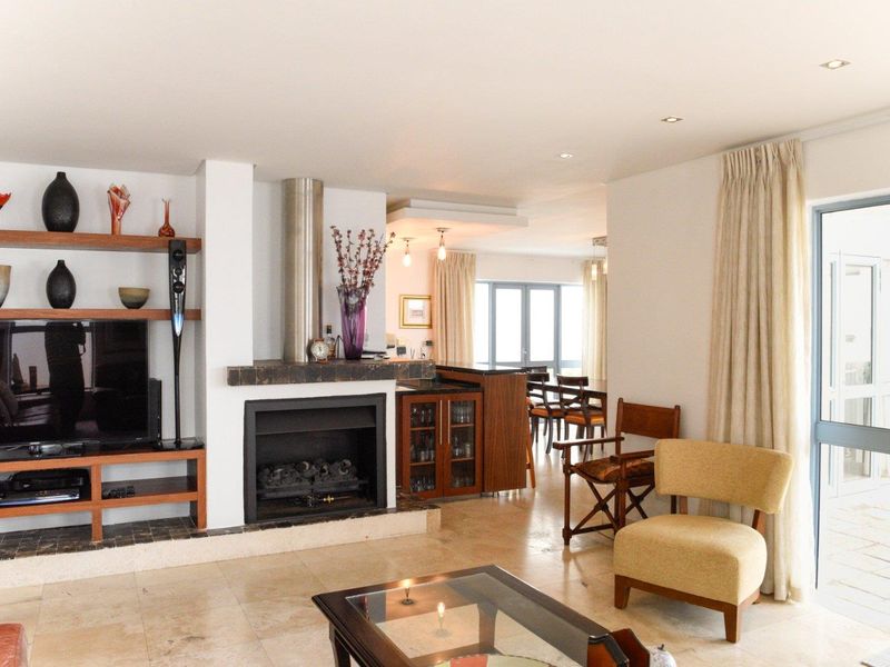 Spacious open-plan living area featuring stone flooring, a built-in fireplace with a stainless steel flue, and direct access to an outdoor patio.