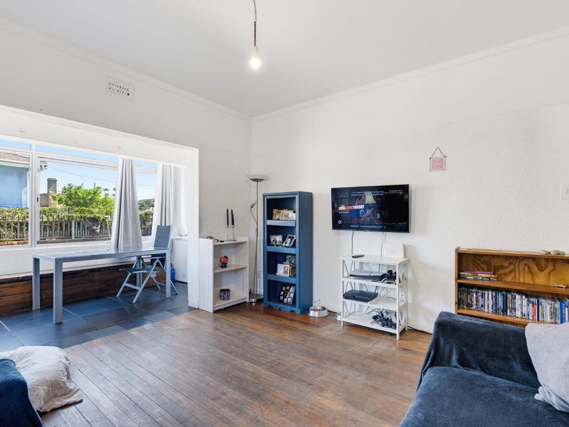 A bright living room featuring original timber flooring, a large window providing natural light, and a wall-mounted television setup.