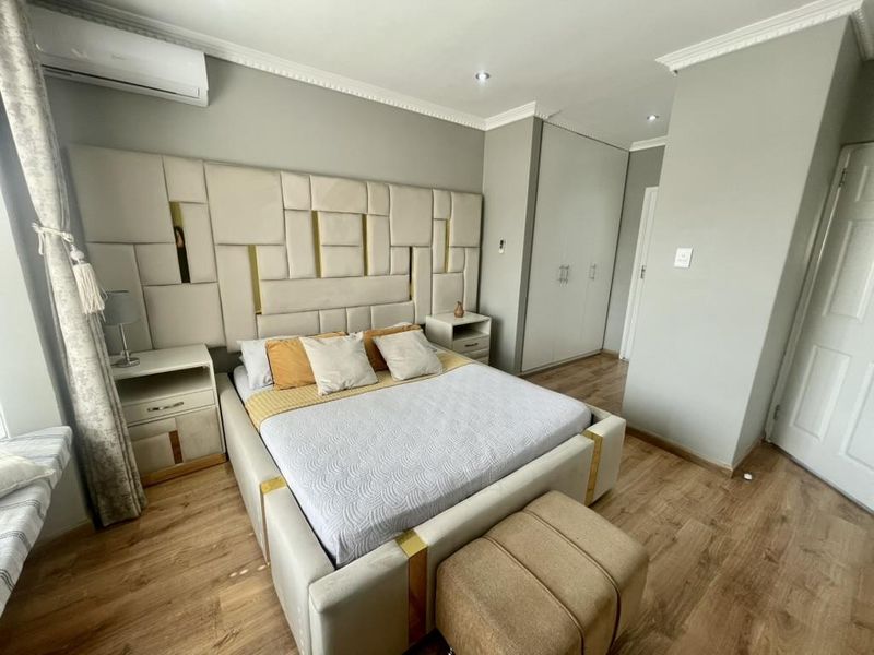 A well-maintained bedroom featuring laminate flooring, built-in cupboards, recessed downlighting, and a wall-mounted air conditioning unit.