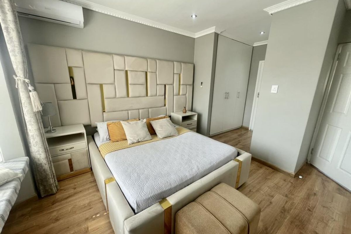 A well-maintained bedroom featuring laminate flooring, built-in cupboards, recessed downlighting, and a wall-mounted air conditioning unit.