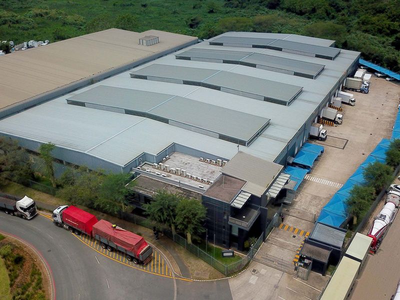 Aerial view of a large industrial warehouse facility featuring multiple loading bays, extensive roof skylights, and secure gated access with parking.