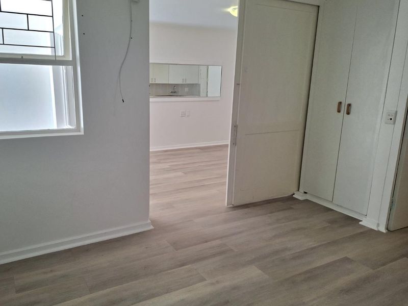 An empty bedroom featuring modern laminate flooring, built-in cupboards, and a sliding door leading to an adjacent living area.