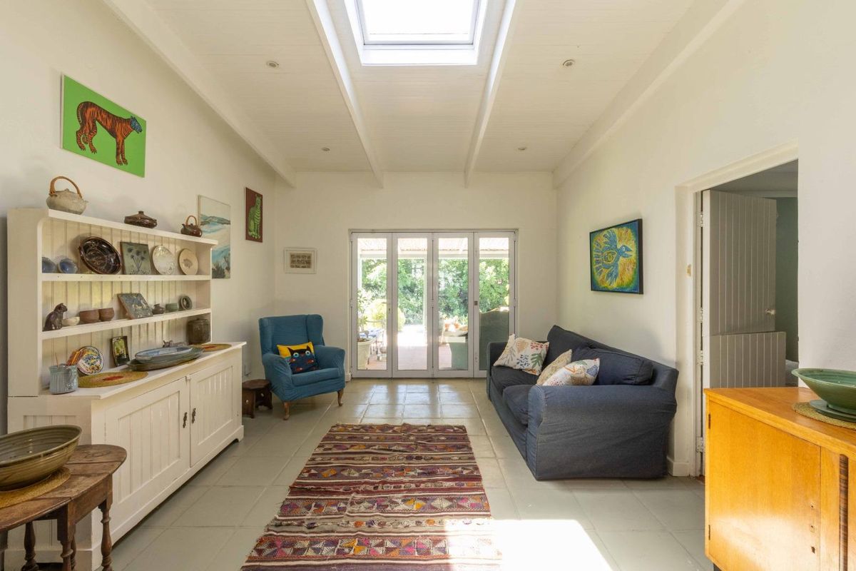A bright living room featuring a vaulted ceiling with a skylight, tiled flooring, and bi-fold doors providing direct access to the rear patio.