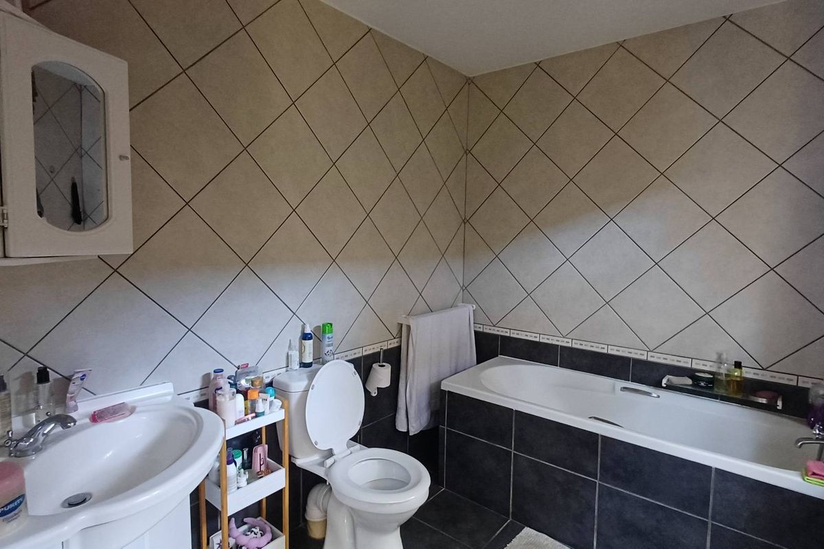 A functional bathroom featuring a pedestal washbasin, toilet, and a built-in bathtub with contrasting wall and floor tiling.