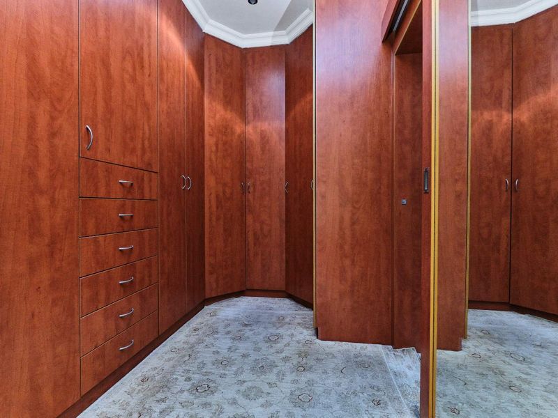 A walk-in dressing room featuring extensive built-in wooden cabinetry with integrated drawers and a full-length mirrored door.