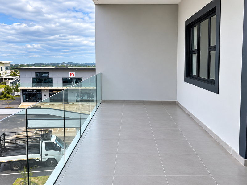 A modern, clean balcony featuring tiled flooring and a sleek glass balustrade, offering an elevated view of the surrounding office park.