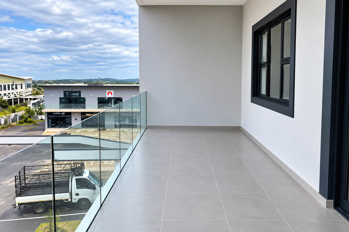 A modern, clean balcony featuring tiled flooring and a sleek glass balustrade, offering an elevated view of the surrounding office park.